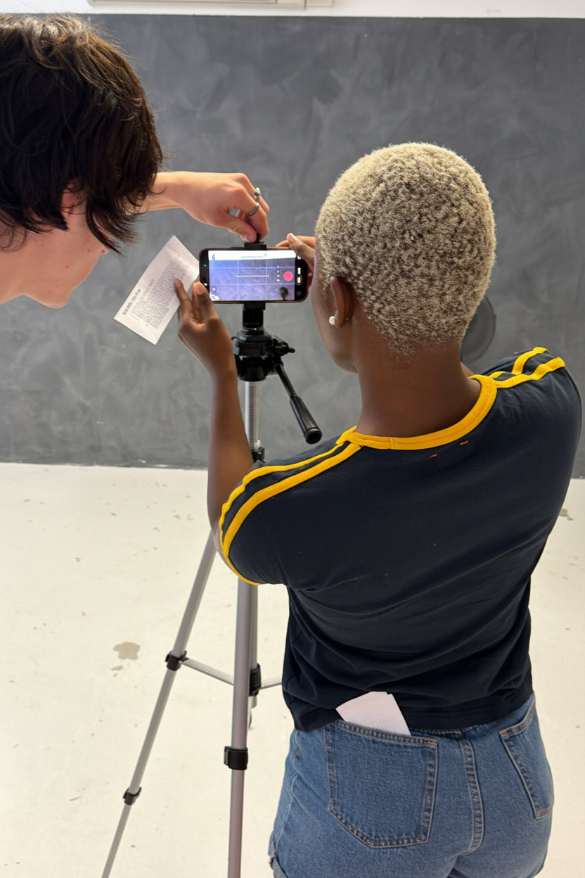 Two people with a smartphone and tripod on a gray floor.
