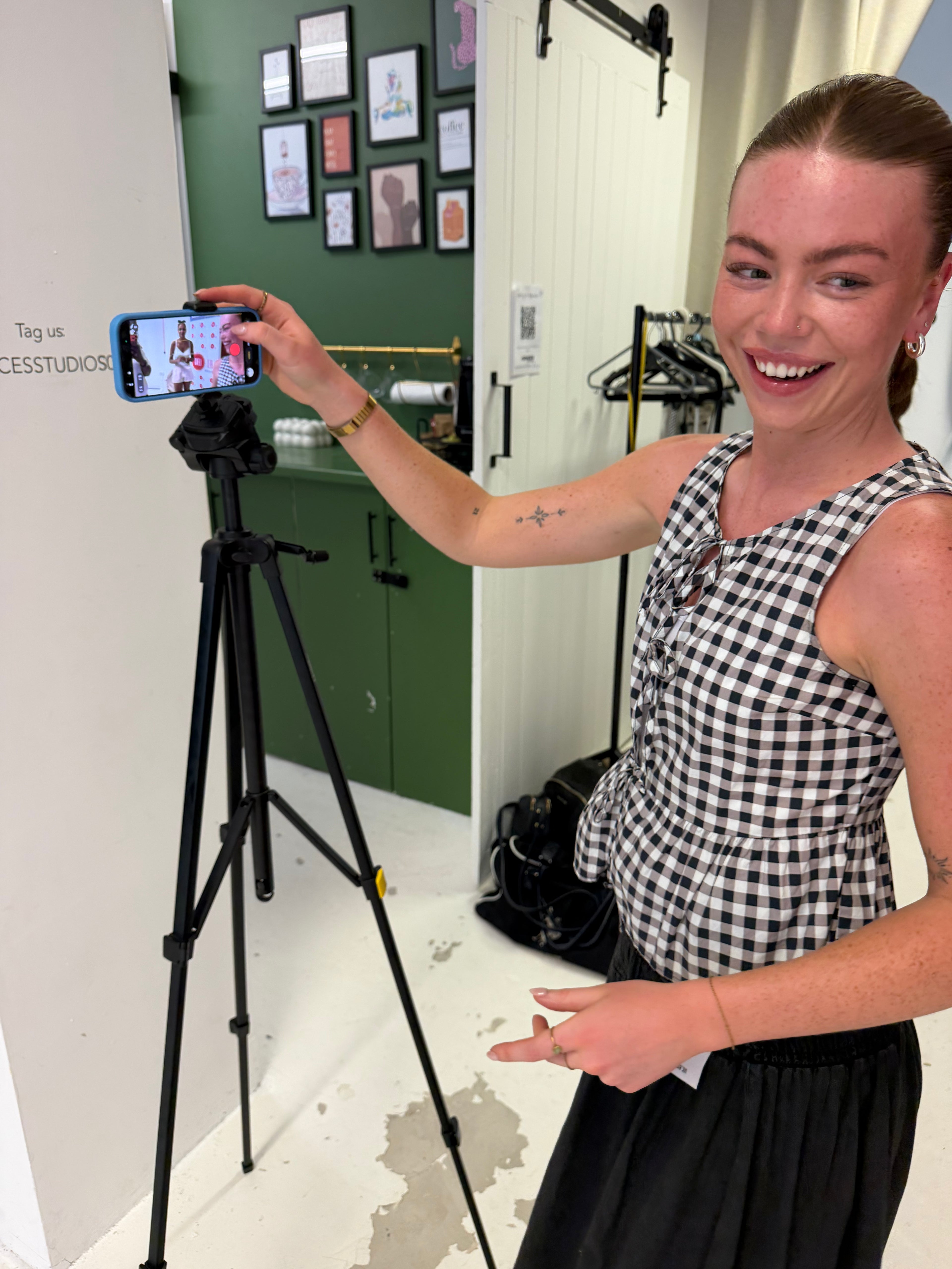 Woman taking a photo of herself on a smartphone with a tripod in a room.